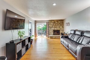 A living room with a stone fireplace, a leather sofa, a flat-screen TV, and a wooden floor. - Kansas City Extended Stay Near Stadiums & Downtown (Kansas City)