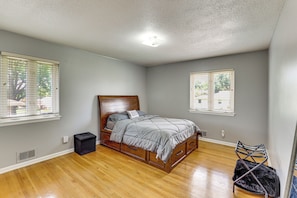 A bedroom with a wooden bed, two windows with blinds, a radiator, and a black storage box. - Kansas City Extended Stay Near Stadiums & Downtown (Kansas City)