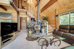 Ein gemütliches Ferienhäuschen im Inneren mit Kamin aus Stein, einem Fernseher, einer Ledersofa und einer Treppe.