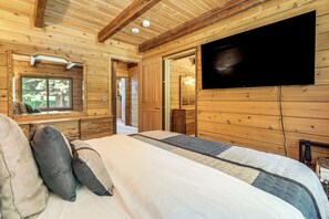Ein Schlafzimmer einer Holzhütte mit einem Bett, Kissen, einem Fernseher und einem Fenster.