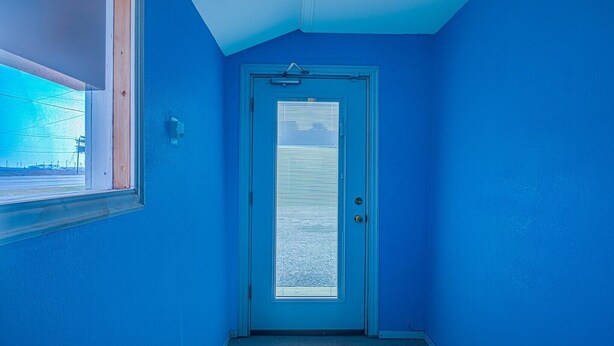 A hallway with a blue door, a window, and a doorbell. - Queen Bed | Non smoking (Corpus Christi TX)