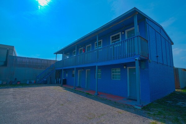 A two-story building with a balcony on the upper floor, a covered entrance, and a gravel driveway.
