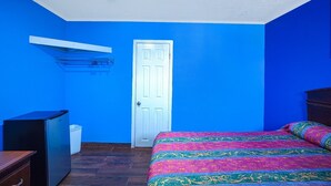 A room with a bed, a door, a shelf, and a small refrigerator. - Queen Bed | Non smoking (Corpus Christi TX)