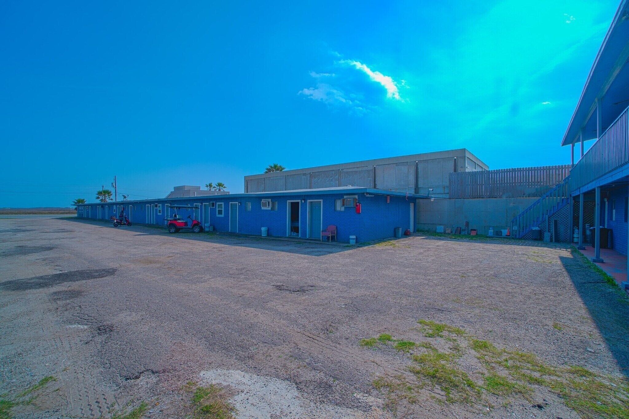 Un bâtiment à la façade bleue, un parking et un ciel dégagé.