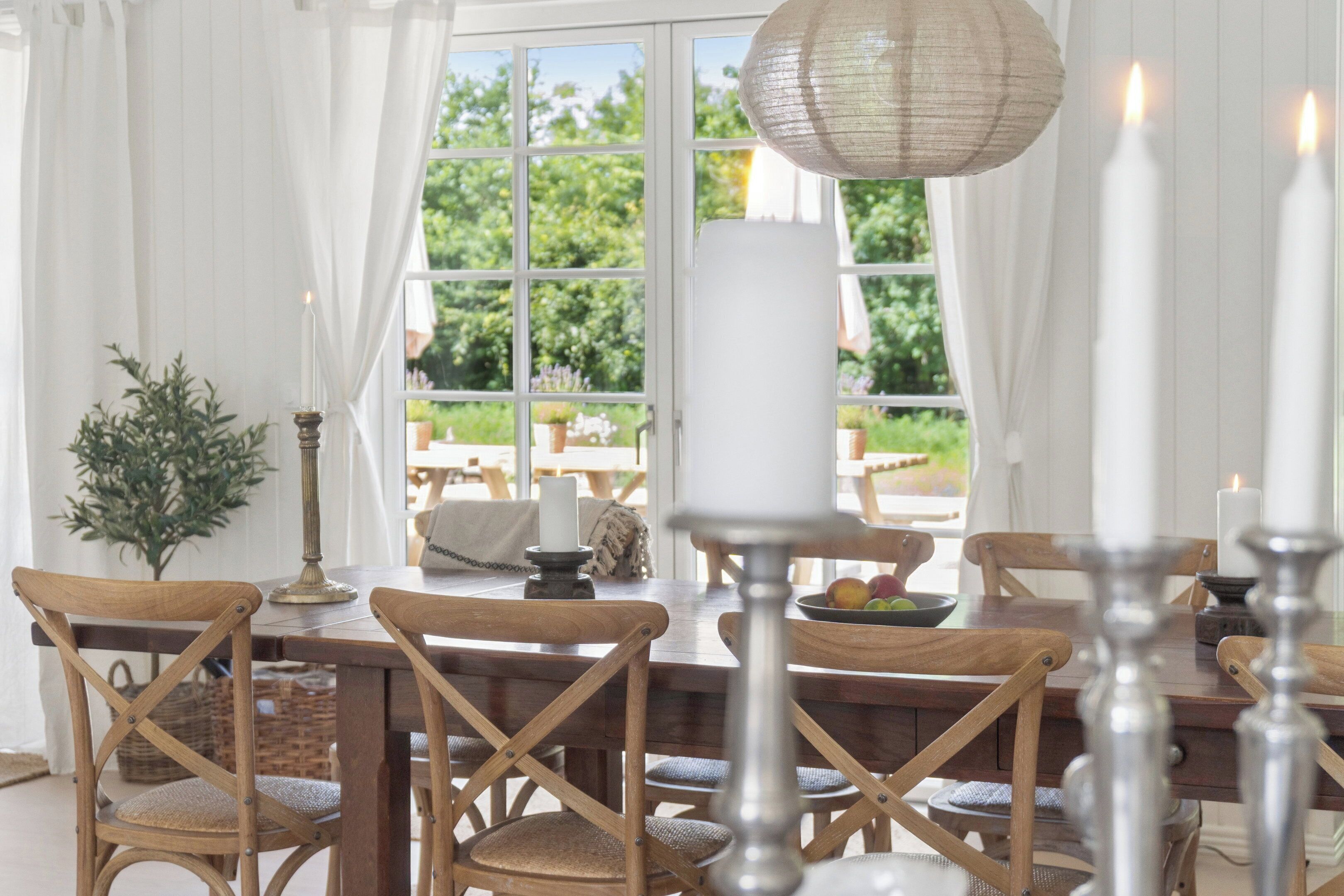 Ein Essbereich mit Holzkstühlen, einem Tisch, Kerzen und Blick durch ein Fenster.