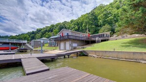 A dock with a wooden walkway leading to a house with a balcony, a small shed, and a grassy hill in the background. - Fire Pit & Floating Dock! Claytor Lake Hideout (Draper)