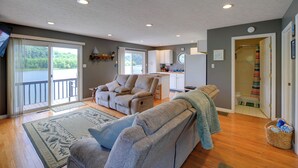 A spacious living area with a sliding glass door to a balcony, a kitchen in the background, and a bathroom with a shower and toilet visible. - Fire Pit & Floating Dock! Claytor Lake Hideout (Draper)