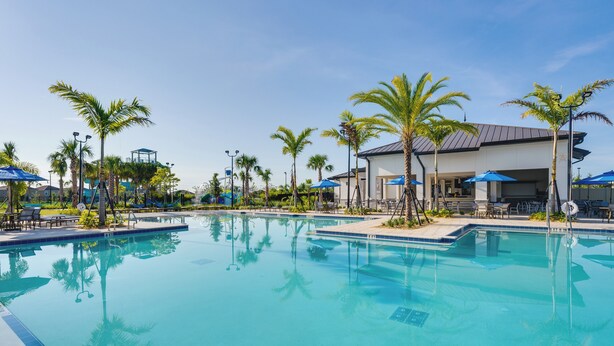 A clear swimming pool with palm trees and umbrellas around it, a covered area with seating, and a building in the background. - 9 Mi to Disney ChampionsGate Condo Plus Water Park (Davenport)