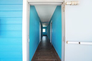 Un pasillo con paredes azules y piso oscuro, que conduce a una puerta con un interruptor de luz y un aplique en la pared.