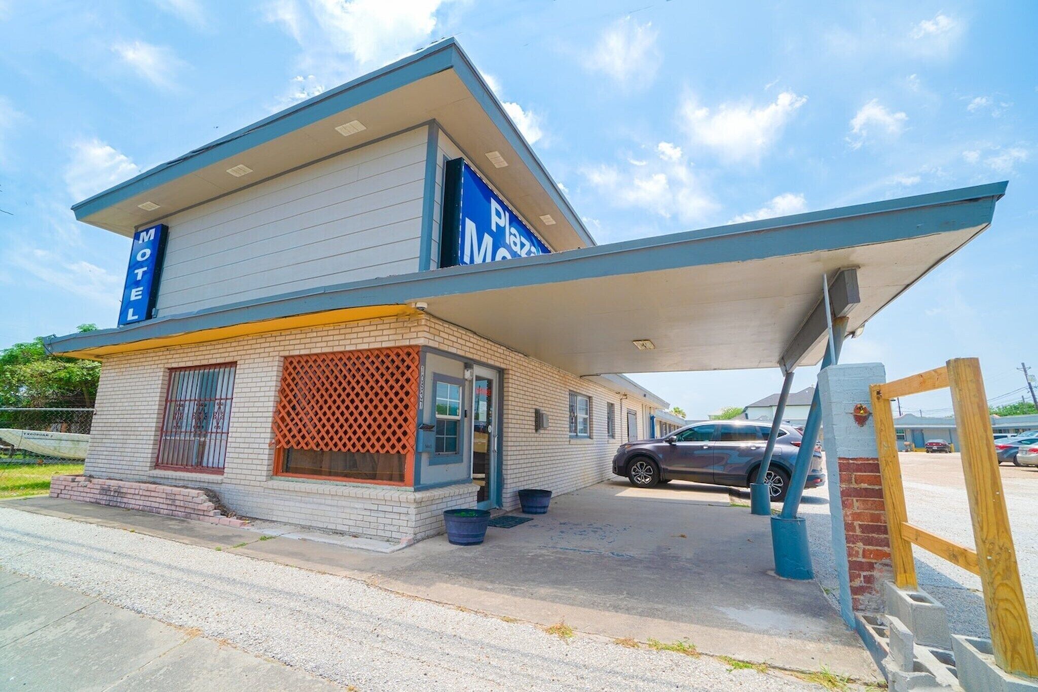 A motel with a two-story structure, a covered parking area, and a visible car in the lot.