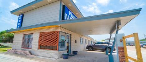 A motel with a two-story structure, a covered parking area, and a visible car in the lot.