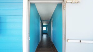 A hallway with blue walls and a dark floor, leading to a door with a light switch and a light fixture on the wall.