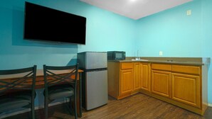 A kitchen with a refrigerator, microwave, wooden cabinets, and a flat-screen TV mounted on the wall.