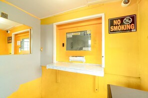 Une salle de bain avec un mur jaune, un panneau « INTERDICTION DE FUMER », une fenêtre avec un panneau « WI-FI GRATUIT » et un miroir.