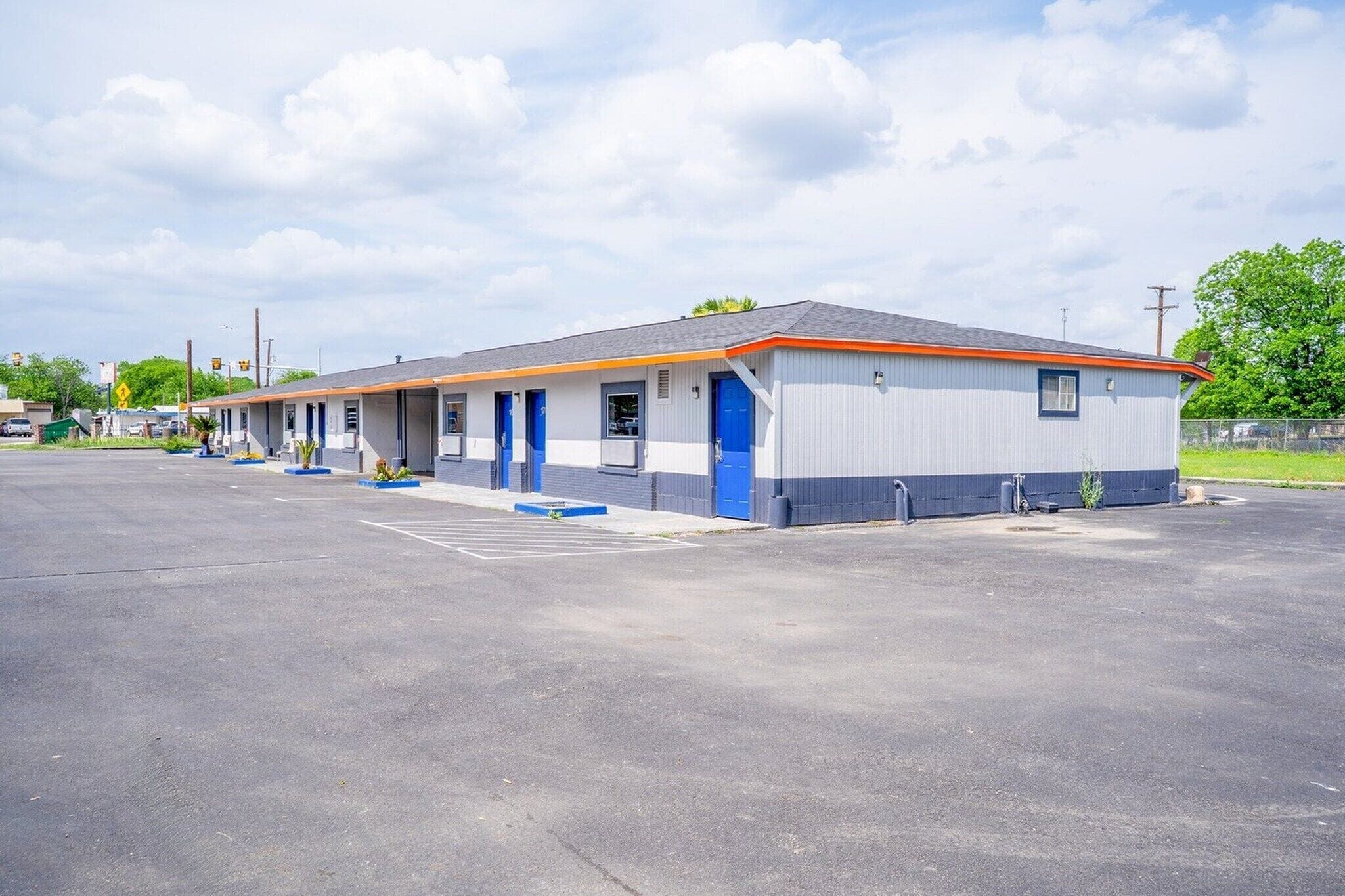Un motel con una hilera de habitaciones, un estacionamiento y cielo despejado.