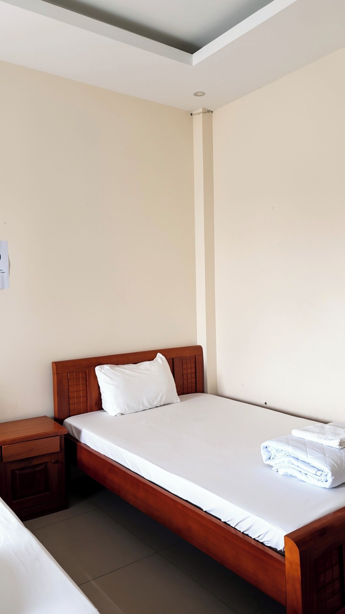 A single bed with a wooden headboard, a nightstand, and a folded towel on the bed.