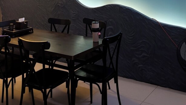 Interior de restaurante con letreros de neón, una mesa, sillas y una pared con diseño de olas.