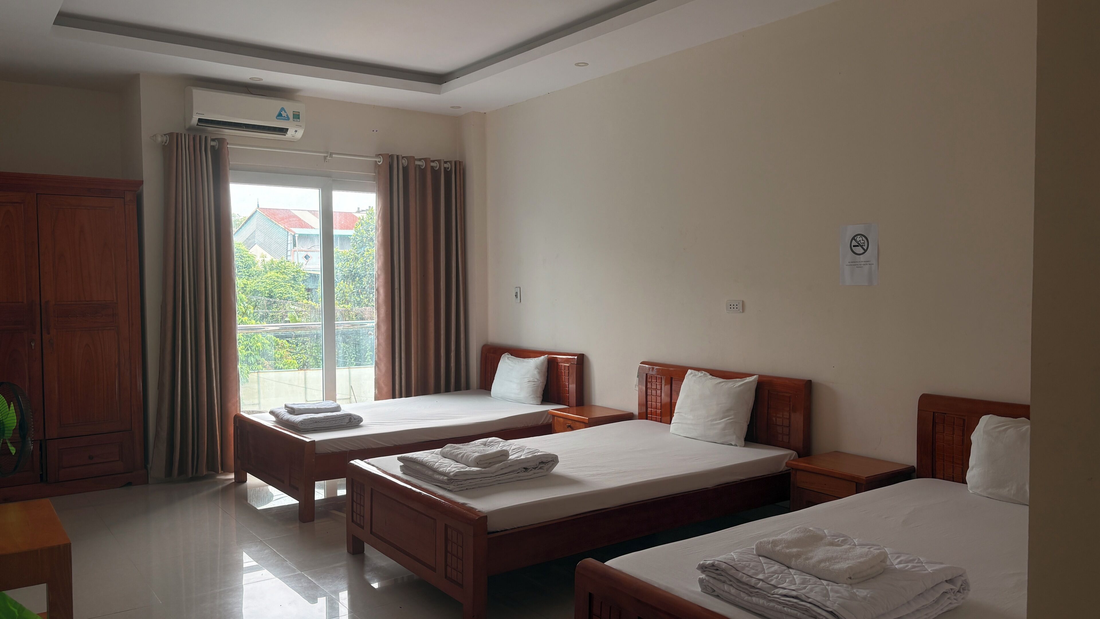 Quarto de hotel com duas camas, um guarda-roupa de madeira, uma janela com cortinas e um aparelho de ar condicionado.