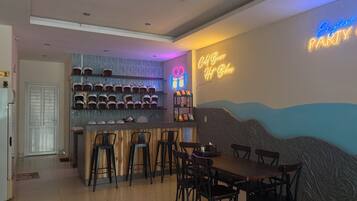 Zona de bar con taburetes y un letrero de neón, una barra con cascos y un letrero luminoso en la pared.