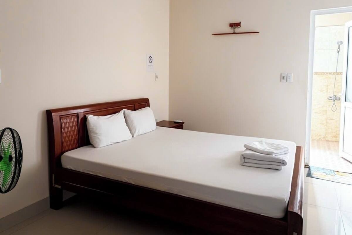 A modern bedroom with a wooden bed, a ceiling fan, and a visible bathroom door.