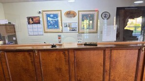 A reception desk with a wooden panel design, framed pictures on the wall, and a clock.