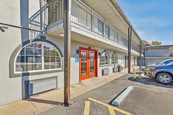 A building with a red door, a handicap accessible sign, and a parking lot with a car. - Queen Bed | Non smoking (Shreveport LA)