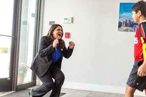 A person in a black suit crouching near a glass door, with a poster advertising a city skyline in the background. - Queen Bed | Non smoking (Shreveport LA)