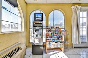 An ATM machine, a magazine rack, and large arched windows in a room with a yellow wall. - Queen Bed | Non smoking (Shreveport LA)