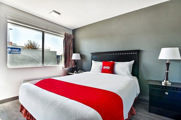 A hotel room with a large bed, a nightstand, a lamp, a window with curtains, and a view of the outside. - Queen Bed | Non smoking (Shreveport LA)