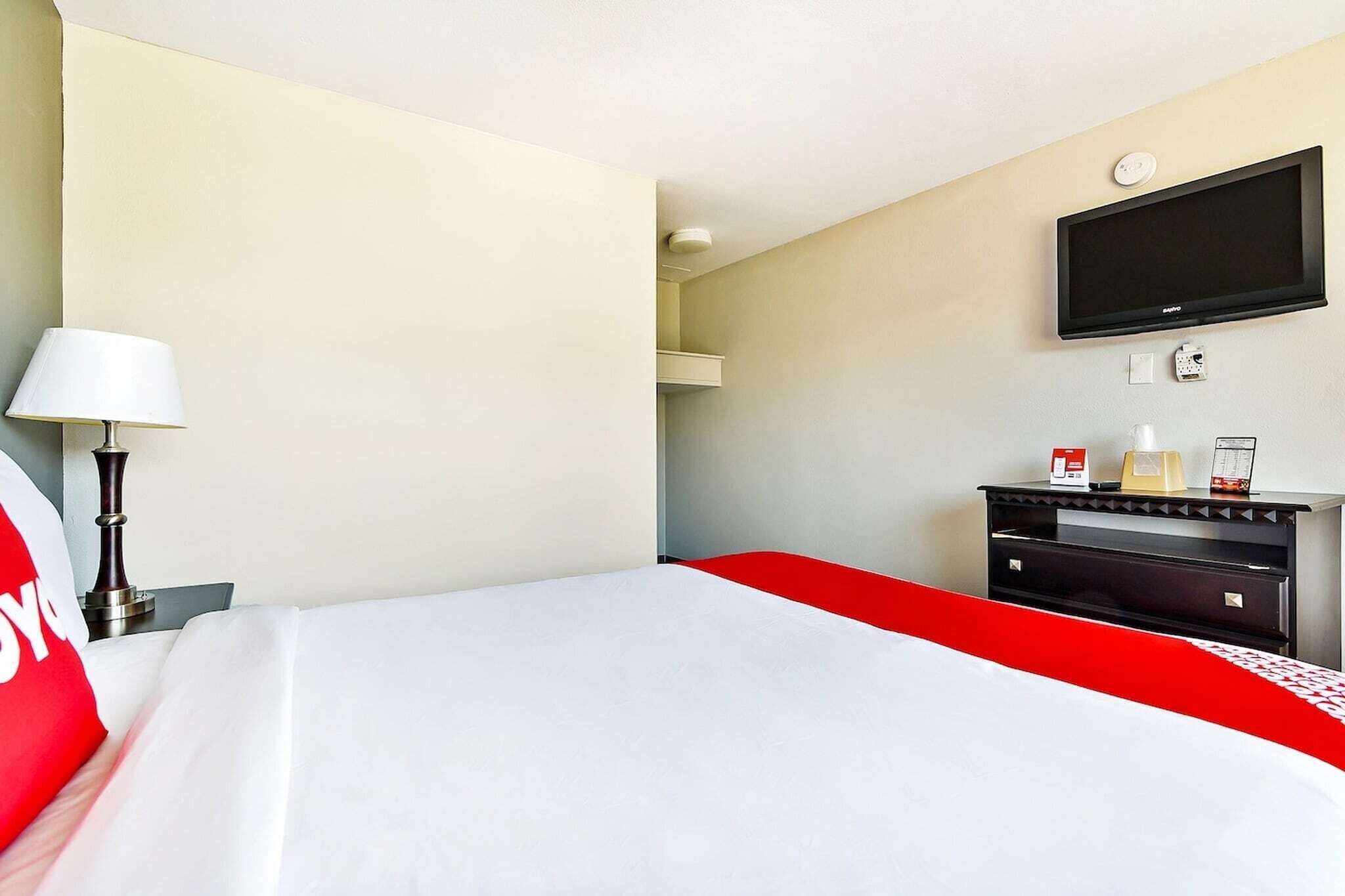 Hotelkamer met een bed, een aan de muur bevestigde televisie, een bureau met een lamp en een minibar.
