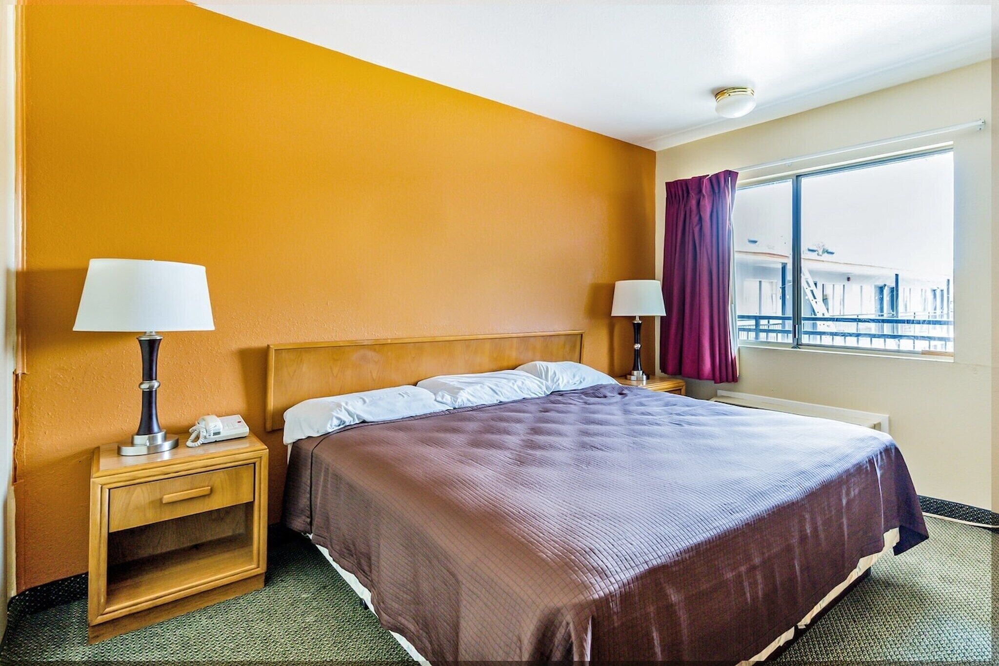 Une chambre d’hôtel avec un lit, deux tables de chevet, une fenêtre avec des rideaux et une vue sur un bâtiment à l’extérieur.