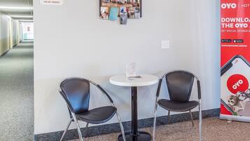 Eine Hotelhalle mit einem Rauchverbotsschild, einem Schwarzdbrett mit Fotos, einem runden Tisch mit zwei Stühlen und einem Werbeplakat für das Hotel OYO.