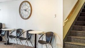 A staircase with a wooden handrail, a round wall clock, and three black chairs with round tables.