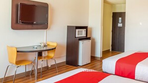 A hotel room with a bed, a desk with a chair, a television mounted on the wall, and a microwave in the corner.