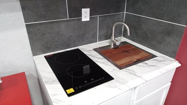 A kitchen with a black induction cooktop, a wooden cutting board, a stainless steel faucet, and a white marble countertop. - King Bed with Kitchenette Non-Smoking (Marshall, MO)