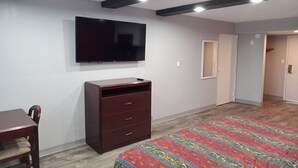 A bedroom with a bed, a dresser, a television, and a door leading to another room. - King Bed with Kitchenette Non-Smoking (Marshall, MO)