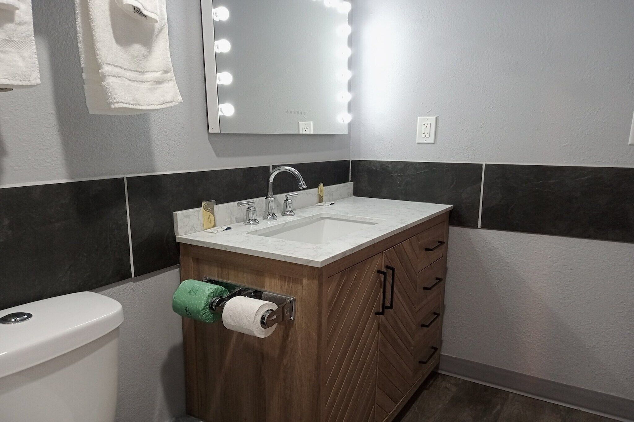 Un baño con tocador, lavabo, espejo con luces y retrete.