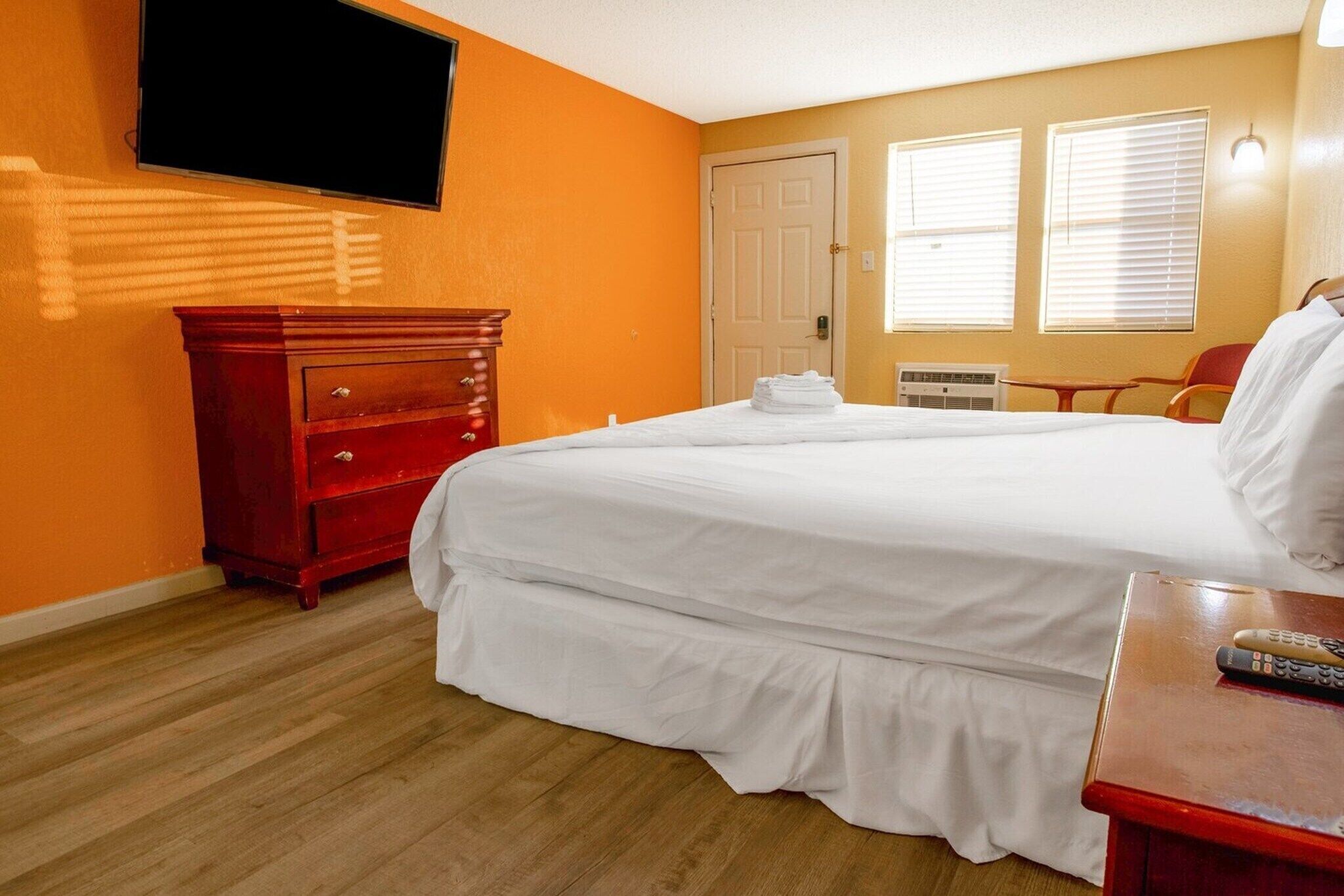 A hotel room with a bed, a dresser, a TV, and a window with blinds.