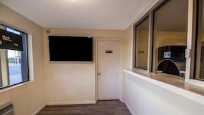 Un pasillo con un televisor de pantalla plana montado en la pared, una puerta con un cartel y una ventana que ofrece vistas al exterior.