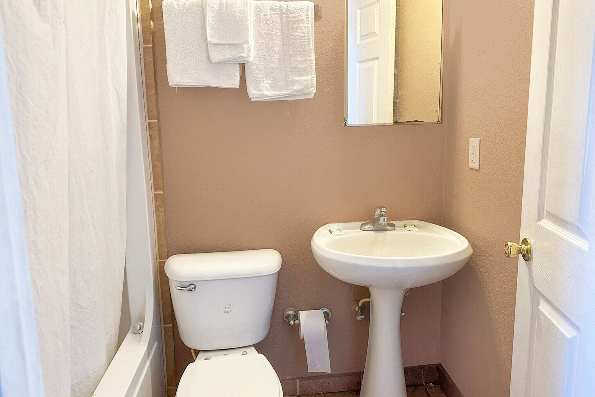 A bathroom with a toilet, sink, and towels hanging on the wall.