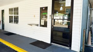A white building with a black door, a window with a sign, and a small outdoor area with a bench. - Premium 2 Queen Bed Smoking (Sparta, GA)