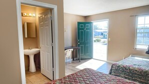 A bedroom with a bed, a window, a door, and a bathroom with a sink and mirror. - Premium 2 Queen Bed Smoking (Sparta, GA)