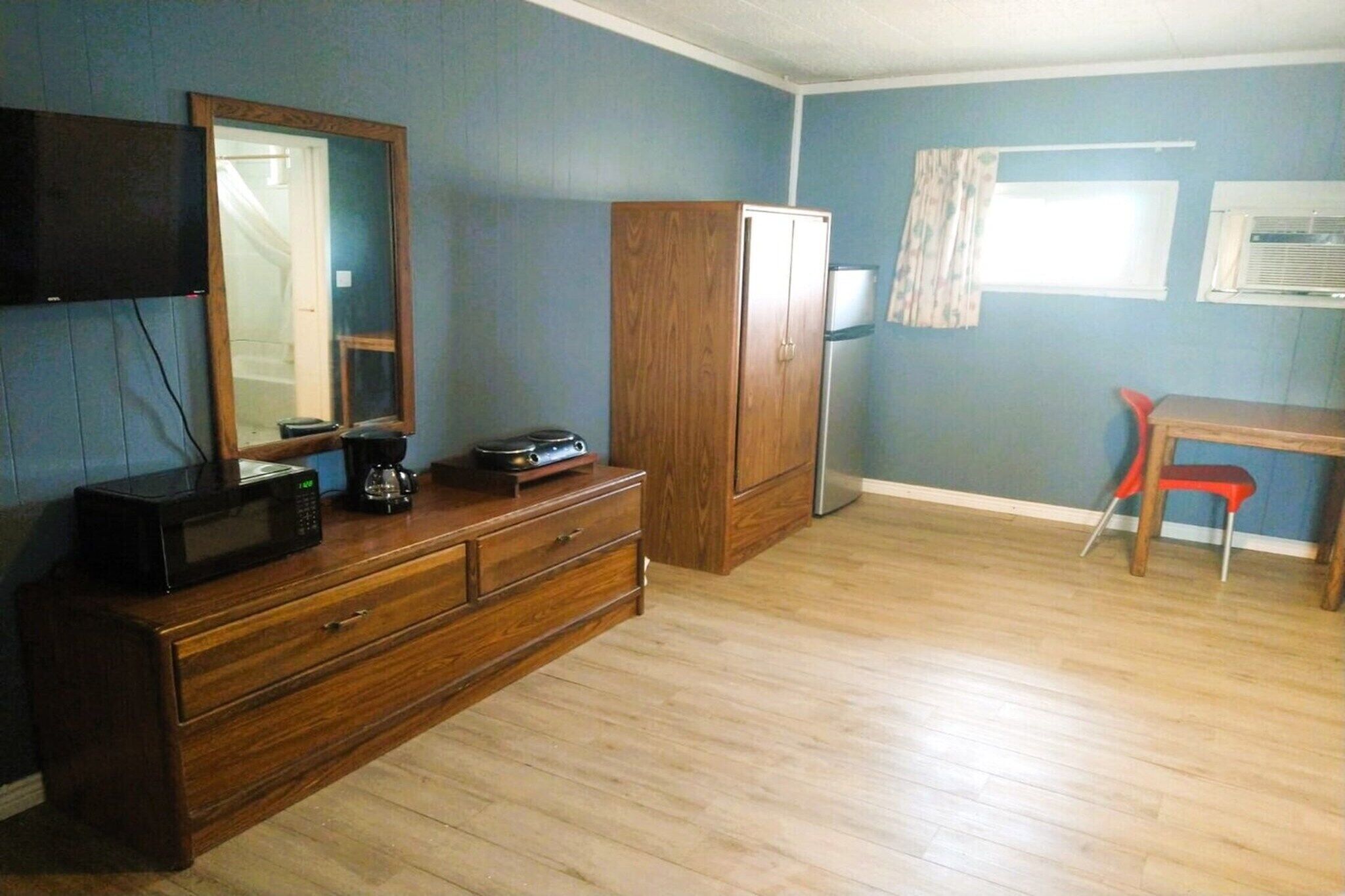 A room with a wooden dresser, a television mounted on the wall, a wooden cabinet, a red chair, and a window with curtains.