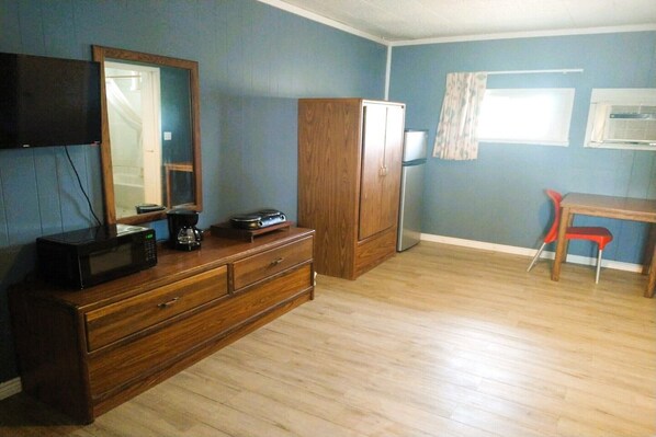 A room with a wooden dresser, a television mounted on the wall, a wooden cabinet, a red chair, and a window with curtains.