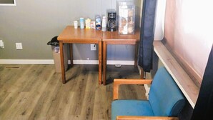 Une petite pièce avec une table en bois, une chaise bleue et une fenêtre avec un rideau.