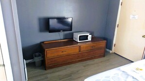 Une pièce équipée d’une télévision, d’un four à micro-ondes, d’une commode en bois, d’une poubelle et d’une porte.