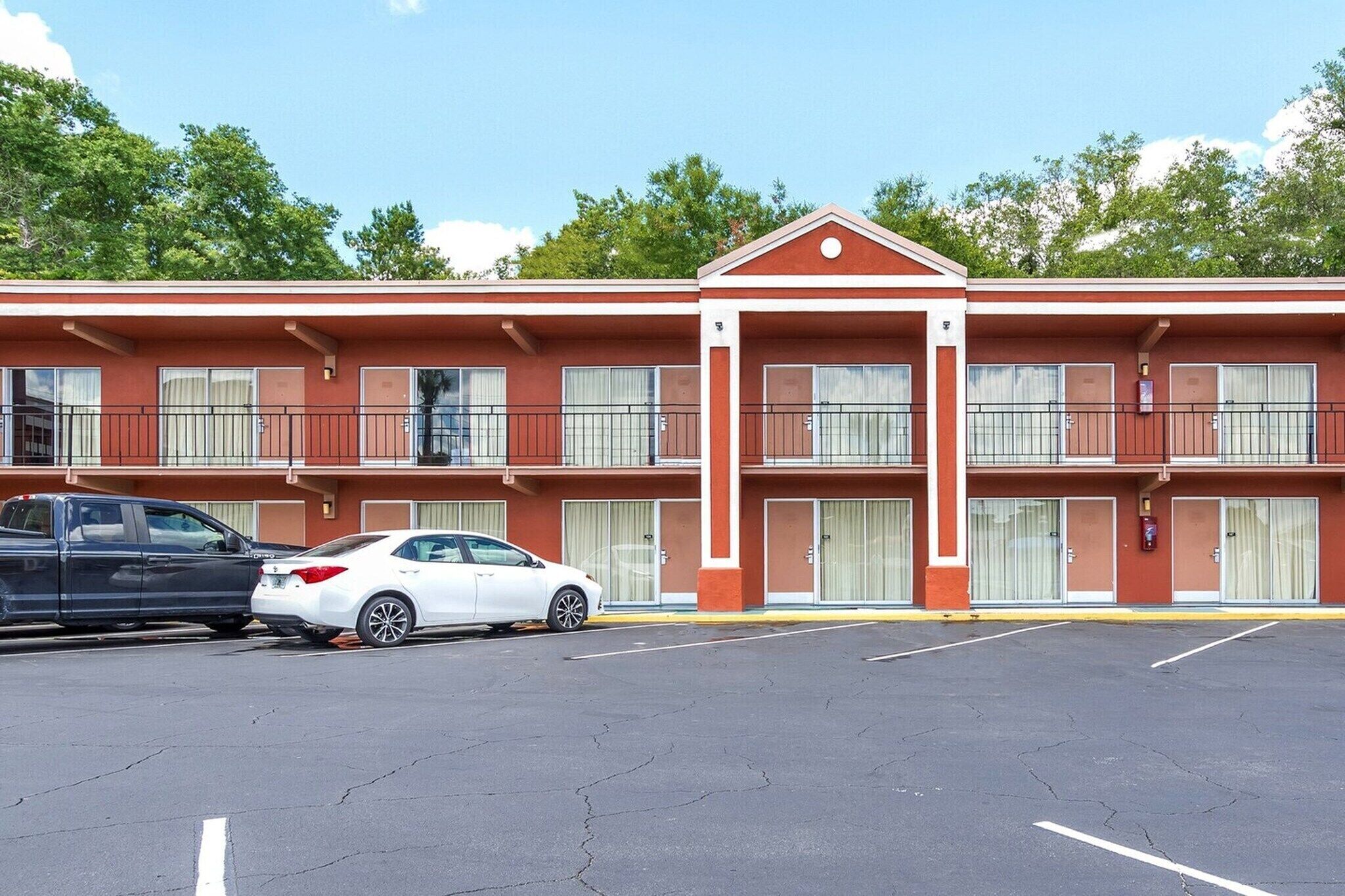 A motel with a red facade, two-story structure, and a parking lot with two cars.
