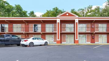 A motel with a red facade, two-story structure, and a parking lot with two cars.