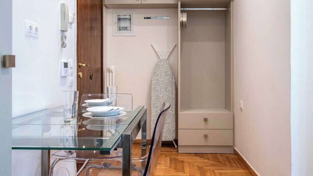 Ein kleines Zimmer mit einem Glastisch, einem Stuhl, einer Kleiderstange und einem Schrank.