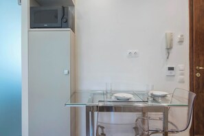 A compact kitchen with a microwave, a glass table with chairs, and a door with a phone and light switch. - Syntagma Gem 2 Steps from Syntagma Square (Athina)